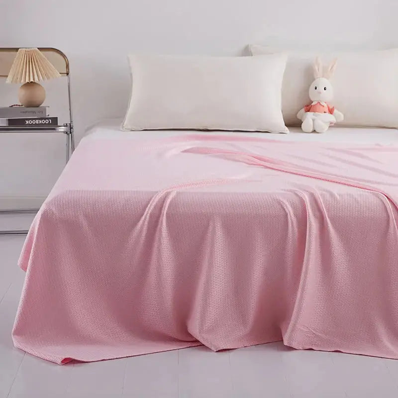Soft pink textured bedspread draped over a bed featuring bamboo fiber summer quilt with diamond grid design