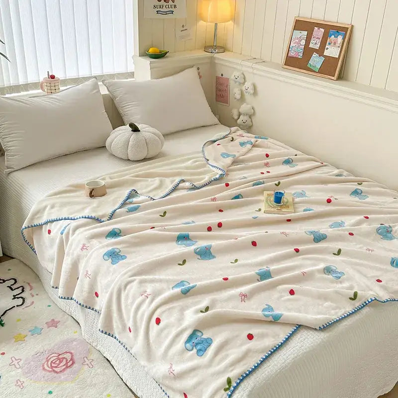 Cream-colored cozy milk velvet blanket with blue elephant pattern and decorative stitched border for travel or bedroom decorbites cozy milk