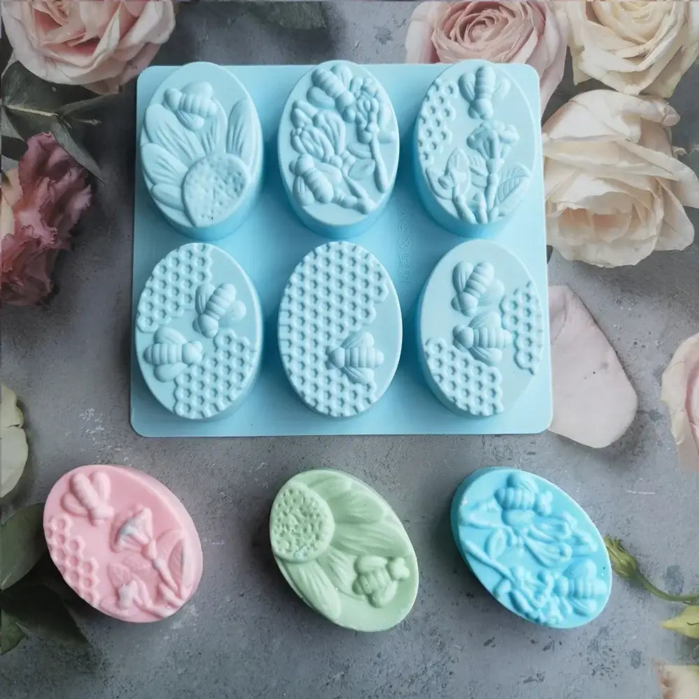Light blue bee silicone soap mold with six oval cavities featuring bee and floral designs and three matching soaps