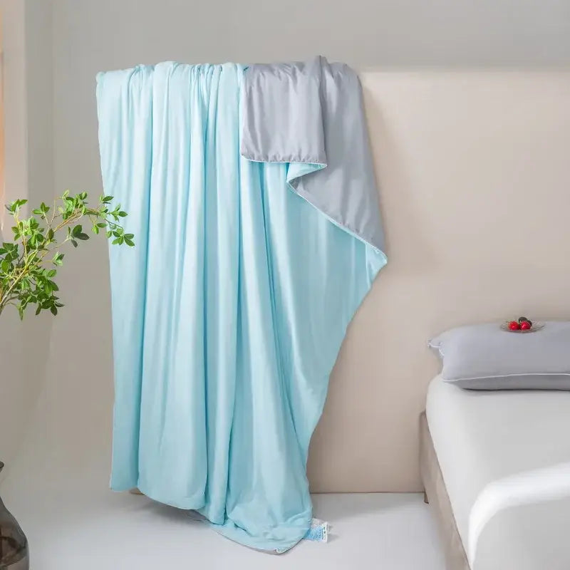 Light blue and gray dual-sided decorbites cool fiber summer blanket draped over a bed for bedroom cooling comfort