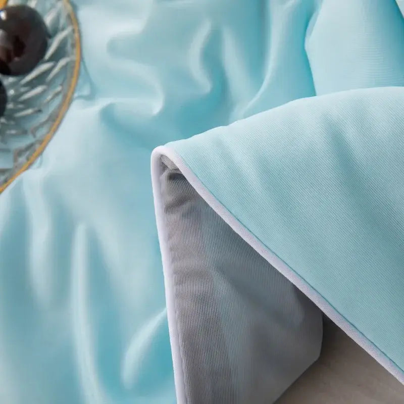 Light blue cool fiber summer blanket with satin-like fabric, white piping, and soft gray inner lining for cooling use