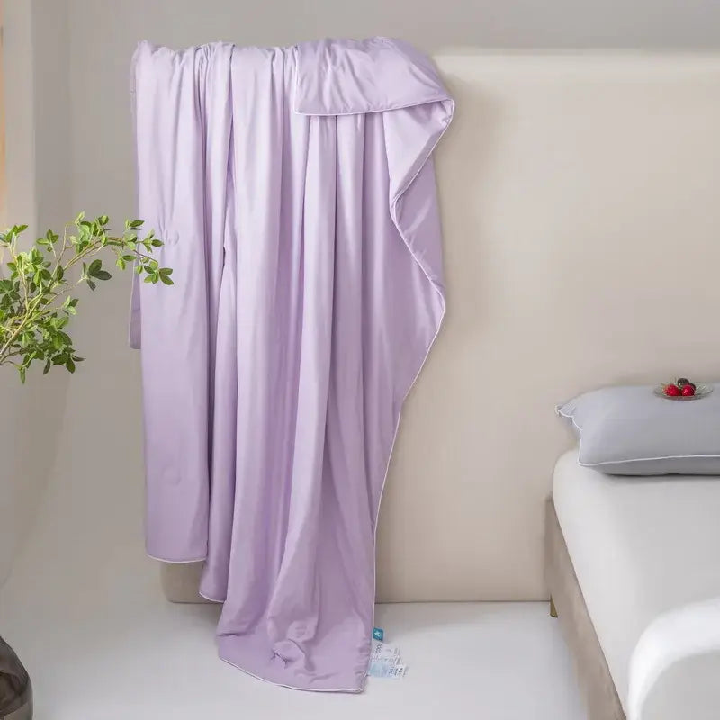 A soft lavender decorbites cool fiber summer blanket with smooth texture draped over a bedhead for cooling comfort