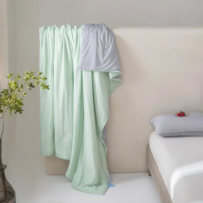 A soft mint green and light gray two-toned decorbites cool fiber summer blanket draped elegantly over a bed