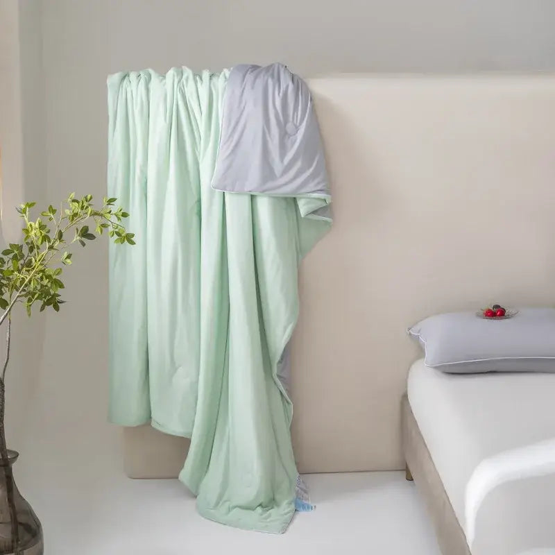 A soft mint green and light gray two-toned decorbites cool fiber summer blanket draped elegantly over a bed