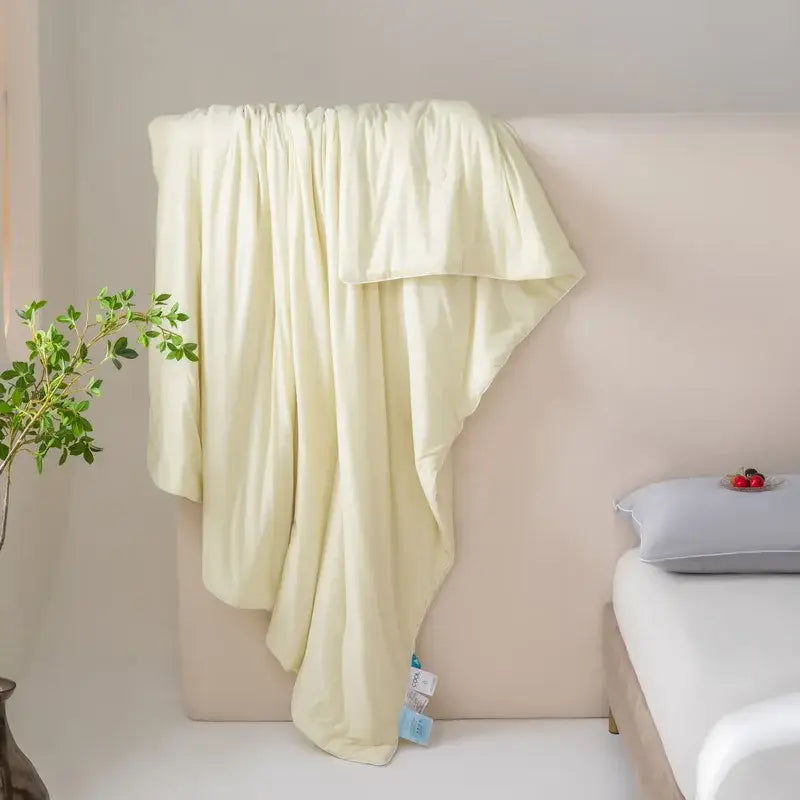 A soft pale yellow silk-like throw blanket draped over a bedhead for decorbites cool fiber summer cooling quilt