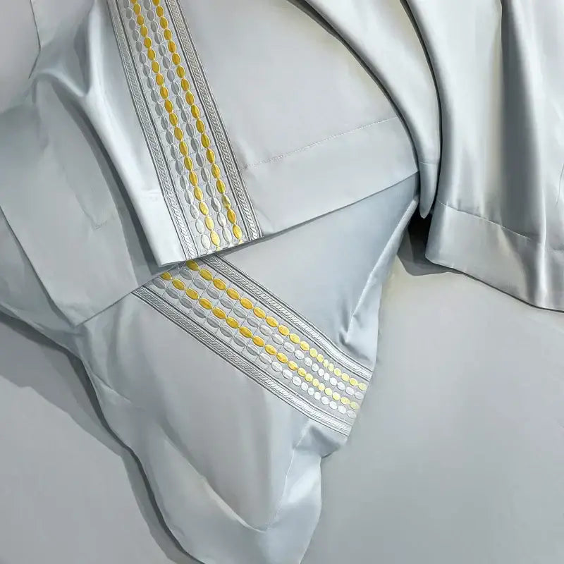 Silver satin pillowcase with elegant gold and silver embroidered stripes complementing light blue egyptian cotton embroidery bedding set