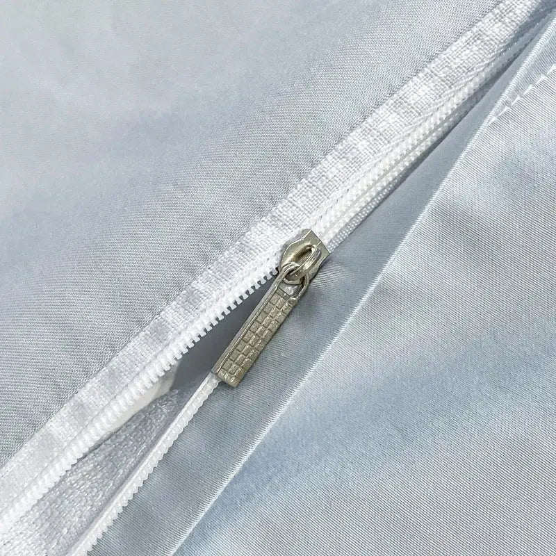 Silver-toned zipper with textured pull tab on light blue egyptian cotton embroidery duvet cover bedding set against gray fabric