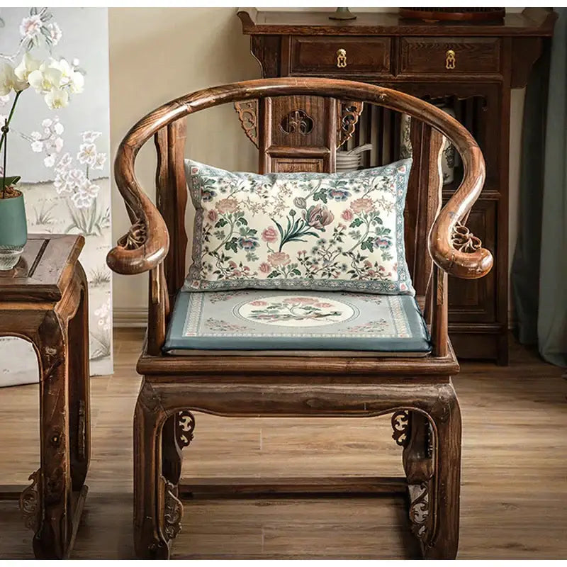 A traditional wooden chair with a light blue flower fragrance pillow cover featuring embroidered floral design