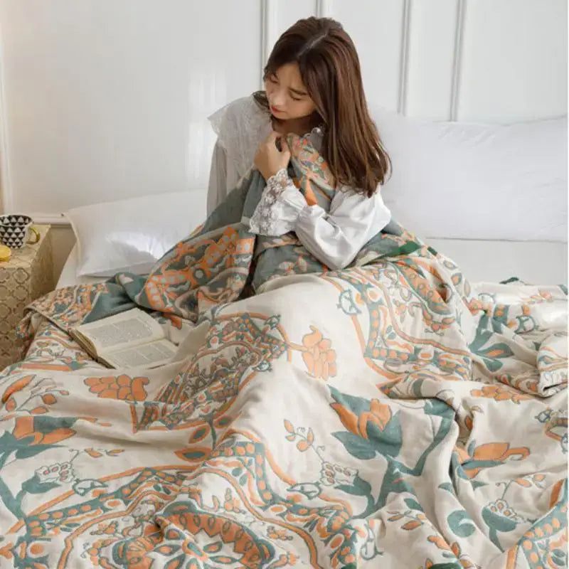 A cream-colored cotton gauze summer blanket with intricate orange and teal floral patterns by decorbites