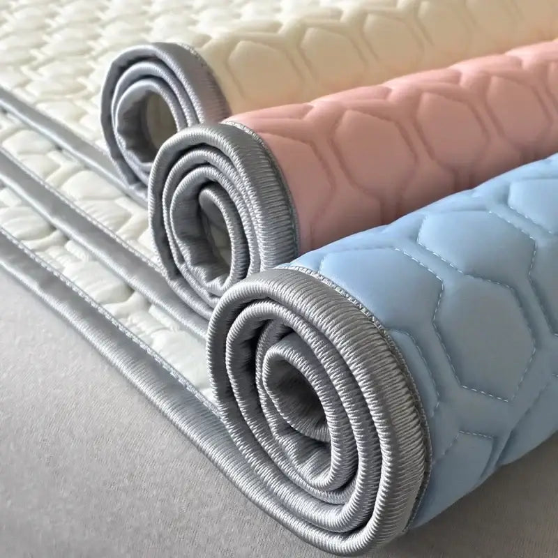 Three rolled-up quilted cooling latex filled bed mats in cream blush pink and light blue with hexagonal stitching