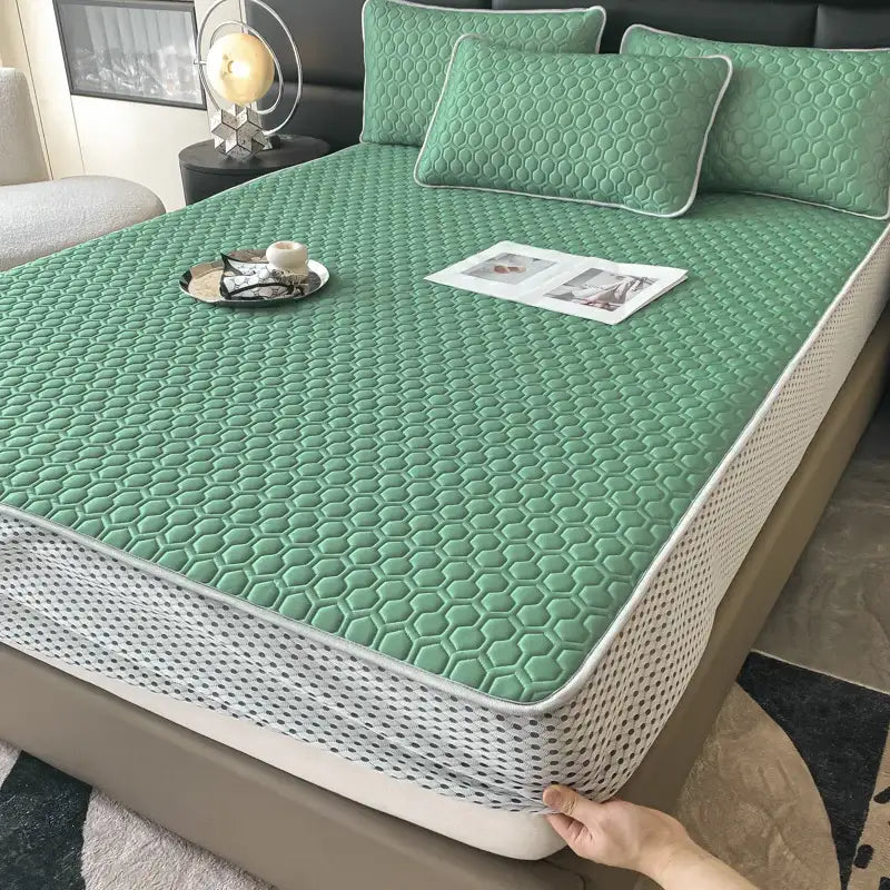 Green hexagonal quilted bed mat with white piping and breathable mesh border in a light blue ice silk cooling mat set