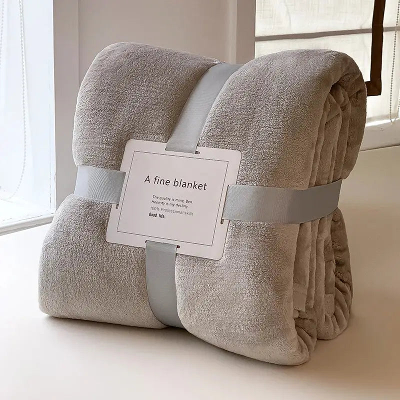 A light gray coral velvet summer blanket plush throw wrapped with light gray ribbons labeled a fine blanket