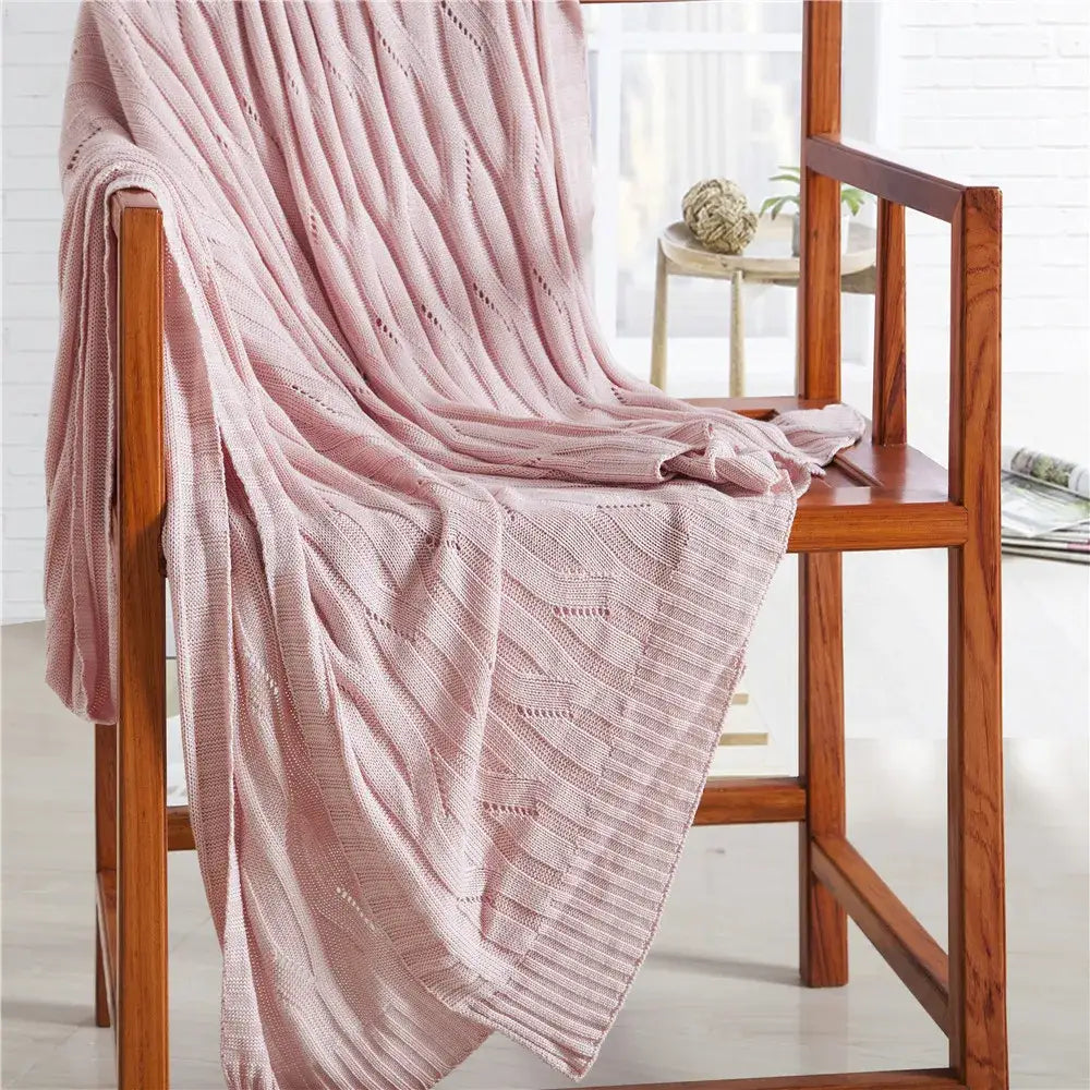 A soft pink bamboo knitted cooling blanket with a ribbed texture draped over a wooden chair for decorbites bedroom use