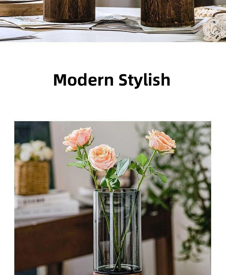 Clear cylindrical glass vase with dark wooden base holding three pink roses for living room table decoration