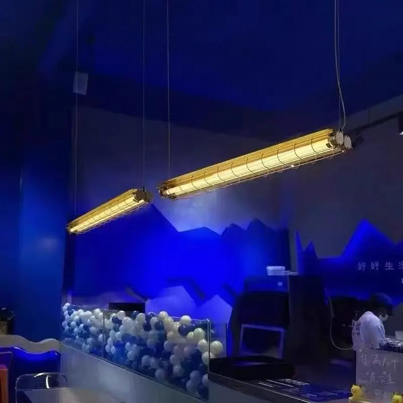 Two hanging industrial-style linear chandelier glass pendant lamps with warm yellow fluorescent lights and metal cages
