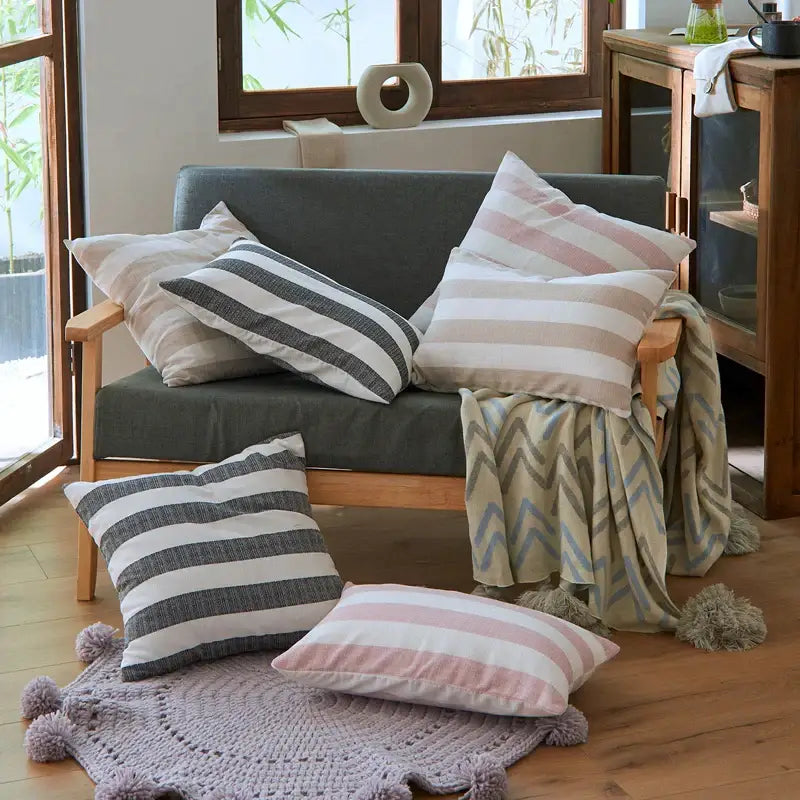 Gray upholstered sofa with wooden arms and legs featuring decorbites linen stripe cushion covers in black-white and pink-cream patterns
