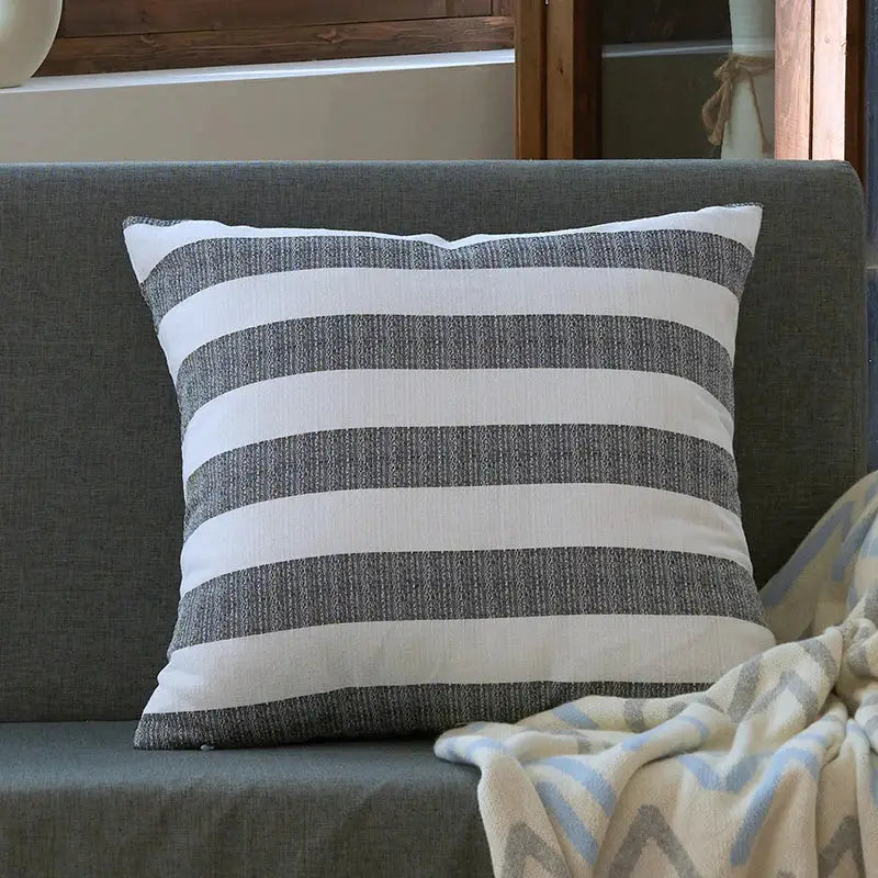 A linen stripe cushion cover with bold gray and white stripes resting on a dark gray couch for living room decorbites linen stripe