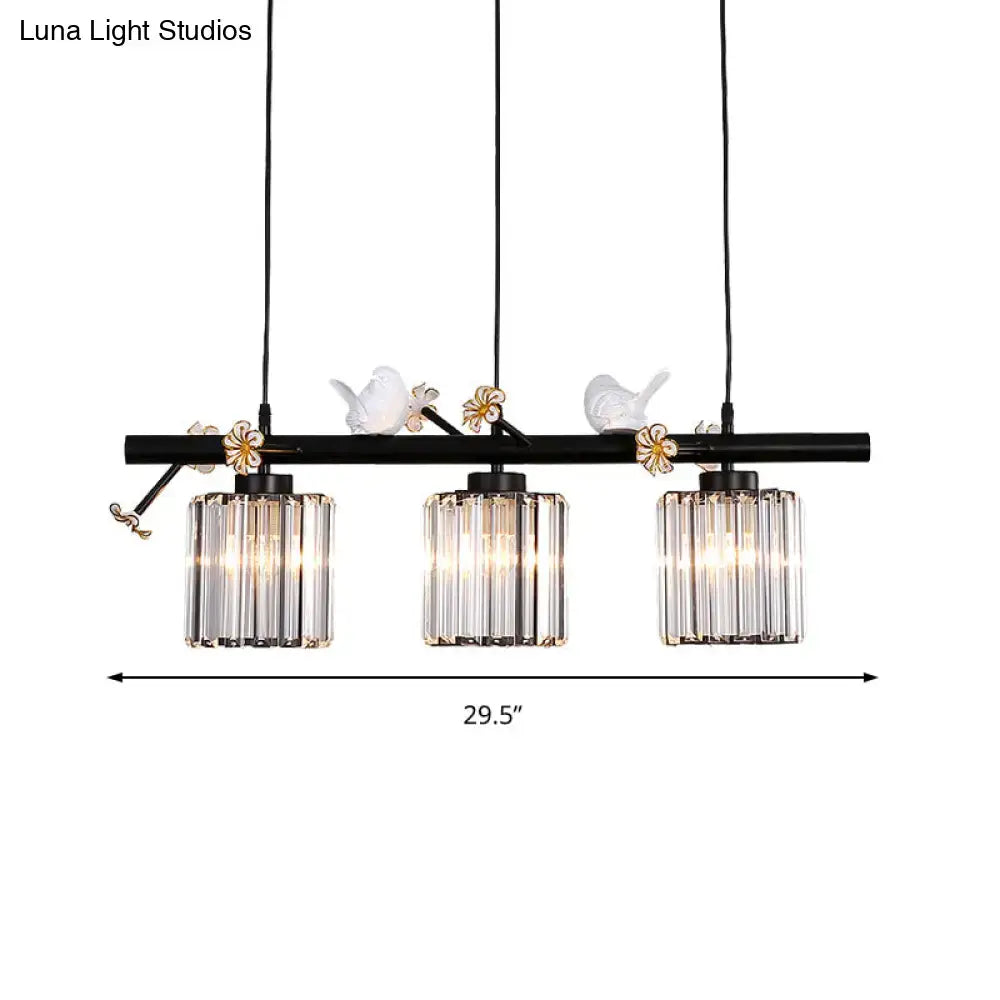 Black wrought iron pendant light with three clear crystal cylinder shades and white porcelain bird accents for island lighting