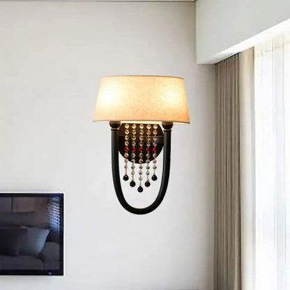 Black wrought iron wall lamp with beige fabric drum shade and crystal bead detail for bedroom decor