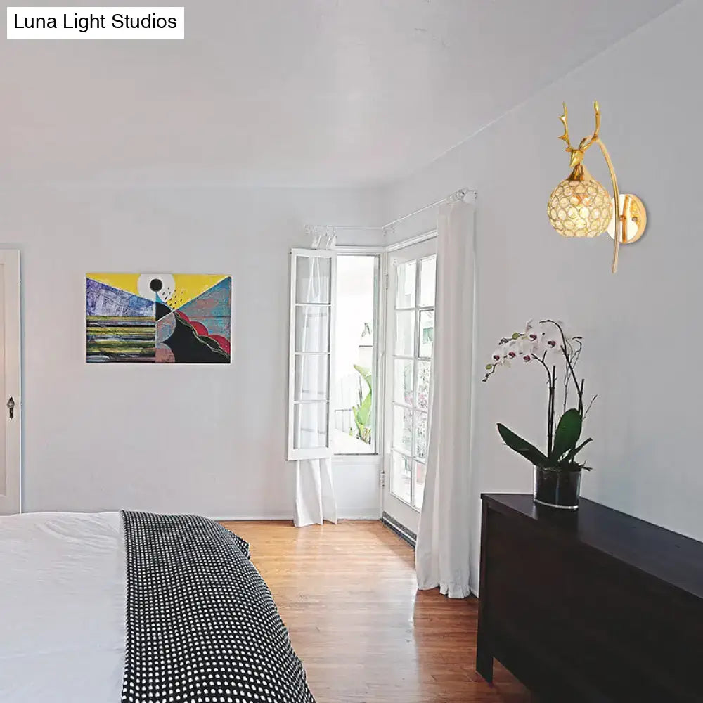 Gold-toned wall sconce with deer antler design and crystal dome shade perfect as a bedroom wall light