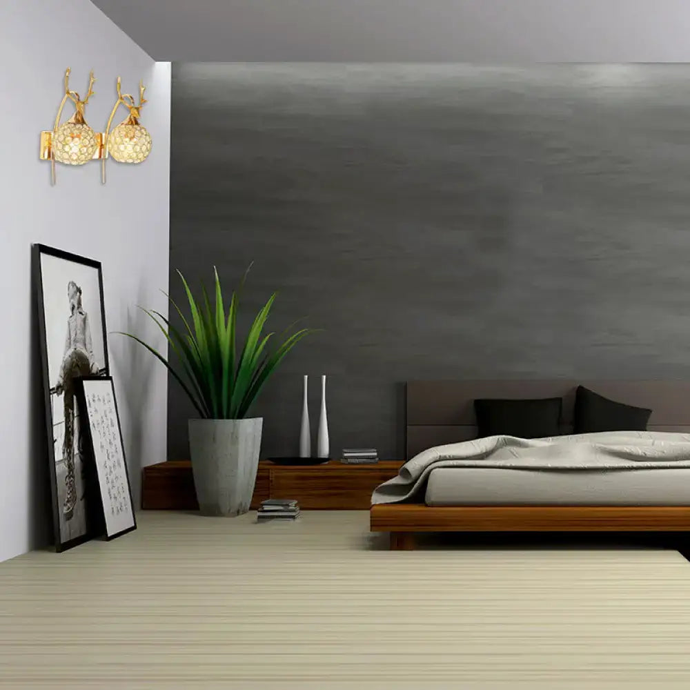 Gold-toned wall sconce with two deer-head fixtures and crystal dome shade for lodge style bedroom wall light