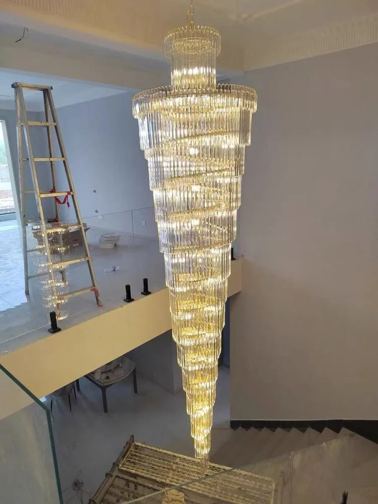 A long crystal staircase gold chandelier with multi-tiered cylindrical design and warm lighting for a hotel hall