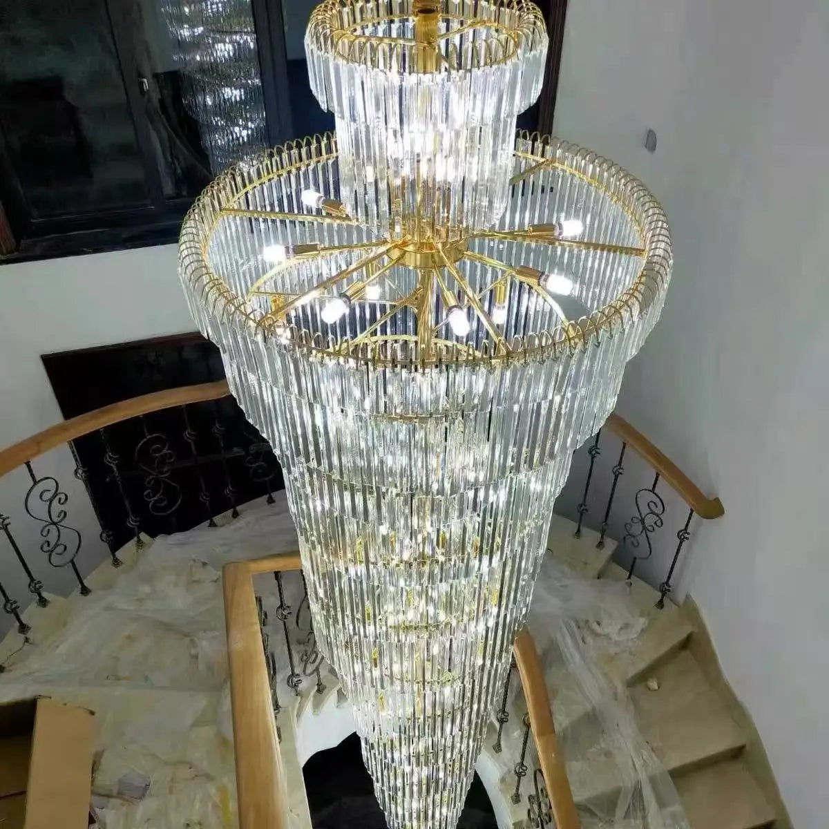 A multi-tiered long crystal staircase gold chandelier with cascading clear crystal prisms for hotel hall decor
