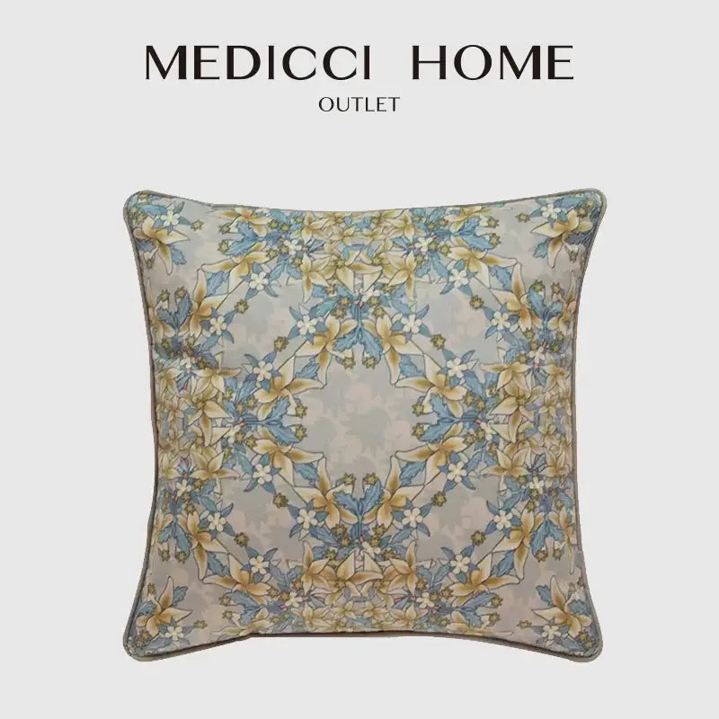 A square luxe blue and gold camellia floral velvet cushion cover from medicci home outlet with an elegant symmetrical floral pattern on beige background