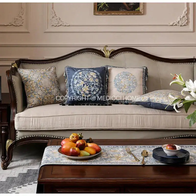 Beige upholstered sofa with dark wood frame and gold accents featuring luxe blue and gold camellia floral velvet cushion cover decorbites camellia floral