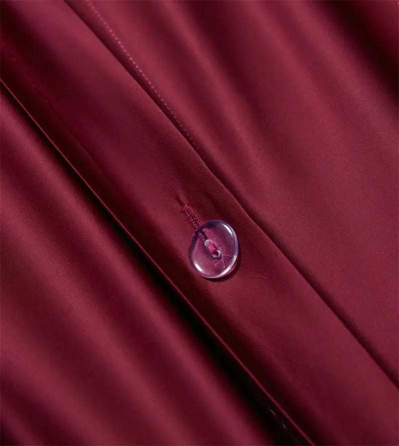 A translucent round button with a pink hue on rich burgundy red egyptian cotton bedding set fabric