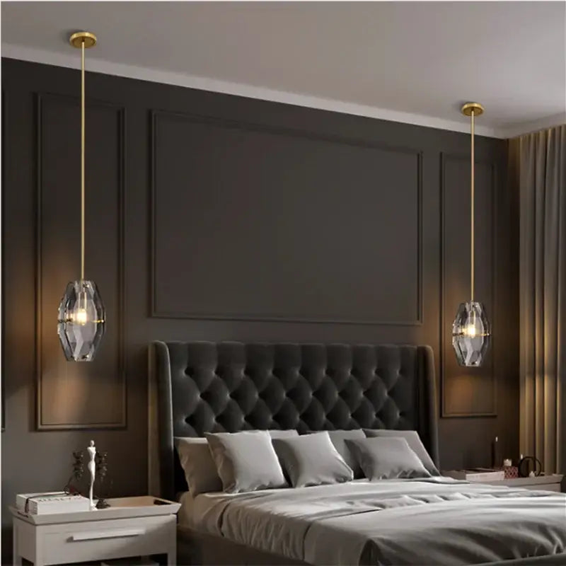Two elegant gold faceted decorbites crystal glass pendant lamps hang symmetrically above a dark tufted bed