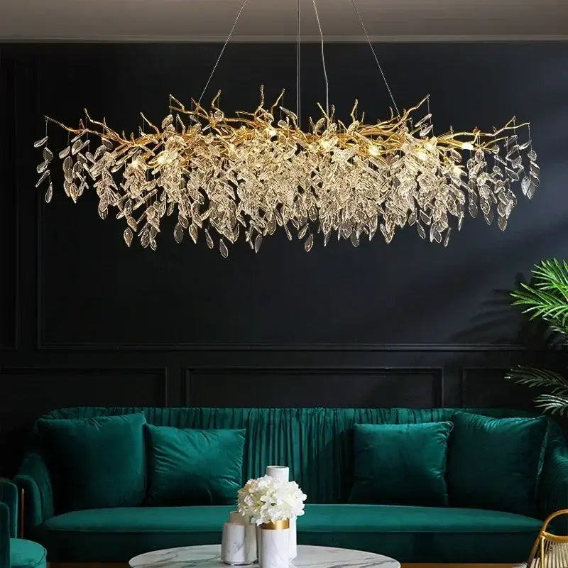 Luxe gold crystal branch pendant light with leaf-shaped chandelier and clear crystal droplets above green velvet sofa
