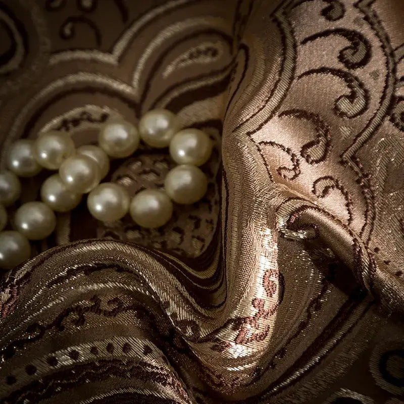 A string of pearls rests on gold and burgundy 200s embroidery Egyptian cotton bedding set fabric