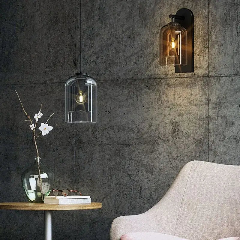 Clear glass bell-shaped wall art light with visible filament bulb hanging from black metal amber sconce fixture