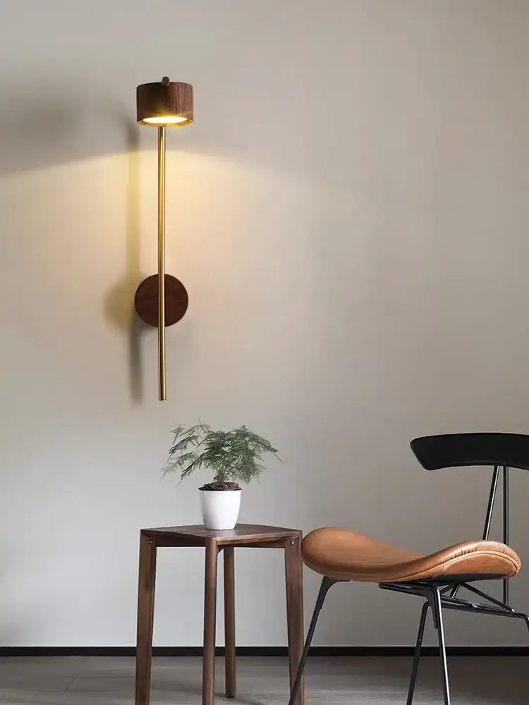 A luxury wall lamp with a brass stem and black walnut wood accents emitting warm light for bedroom reading