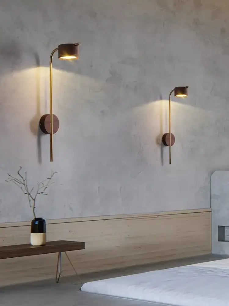 Two minimalist brass wall lamps with black walnut wood bases and warm glow for bedroom reading light