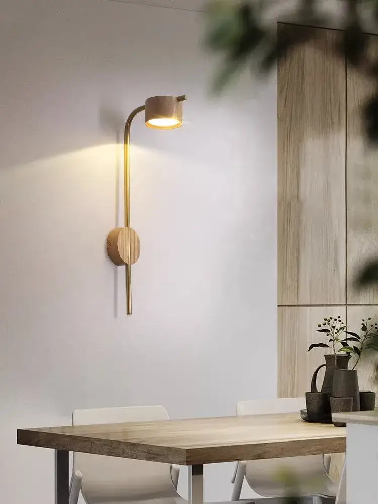 A sleek brass wall lamp with black walnut wood circular base and curved arm emitting warm light for bedroom reading