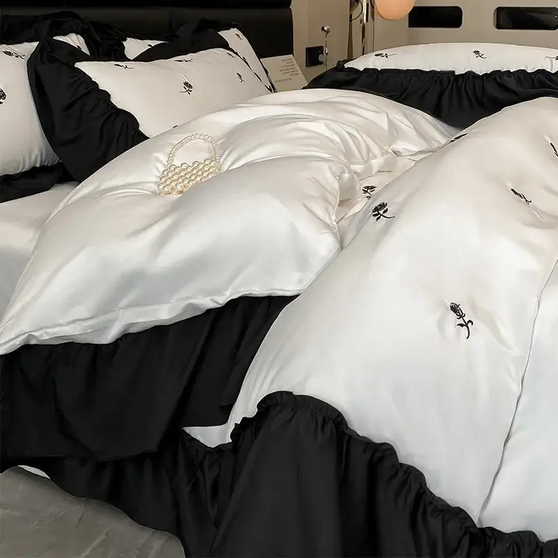 Luxury cream and pink ice silk bedding sets featuring a white satin duvet cover with black ruffled trim and embroidered roses
