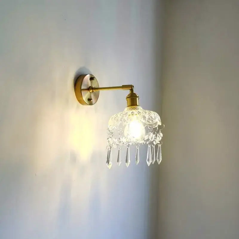 A delicate crystal copper led wall sconce with brass finish glass shade and dangling crystal teardrops for bedroom lighting