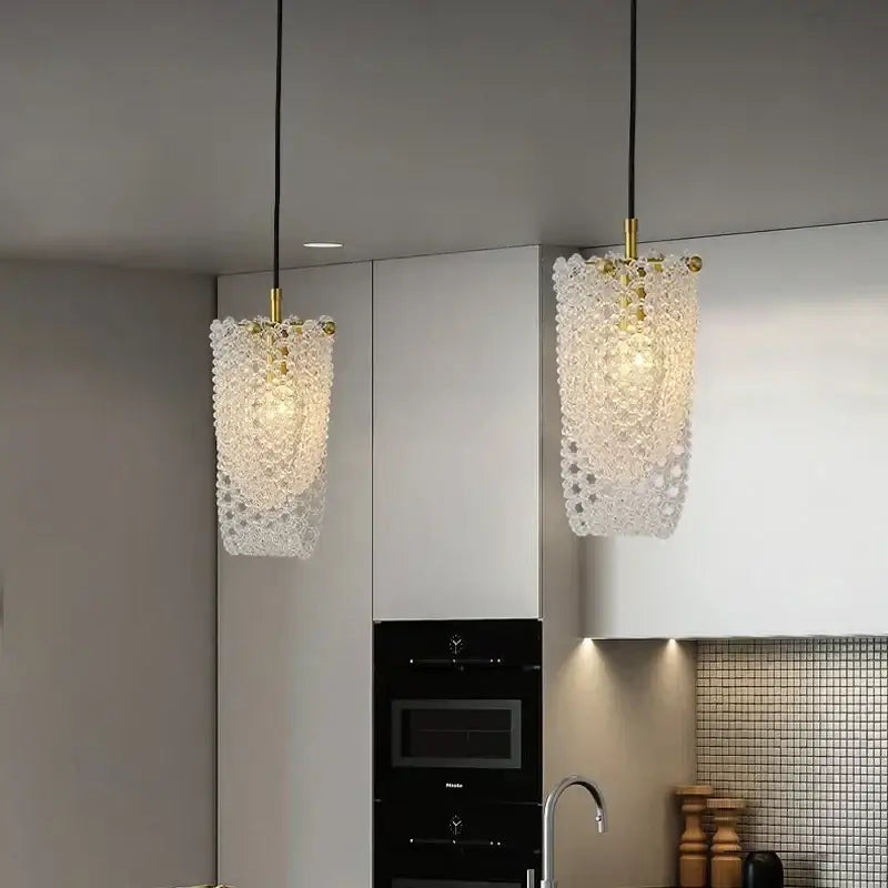 Two elegant crystal tassel pendant lights with gold fixtures hang above a modern kitchen counter