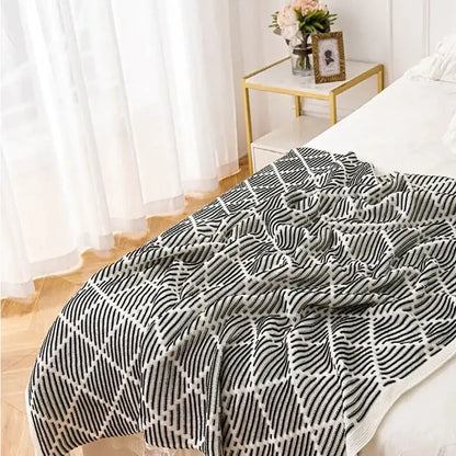 A cozy black and white geometric-patterned decorbites knit sofa blanket with pom poms draped over a bed