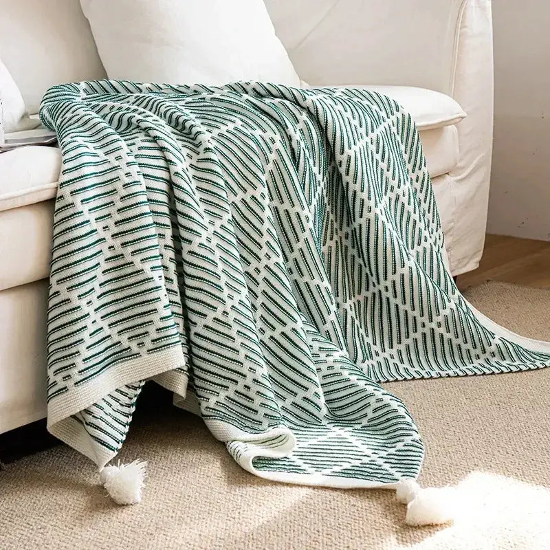 Luxury plaid decorbites knit sofa blanket in soft green and white with geometric pattern and fluffy pom pom tassels
