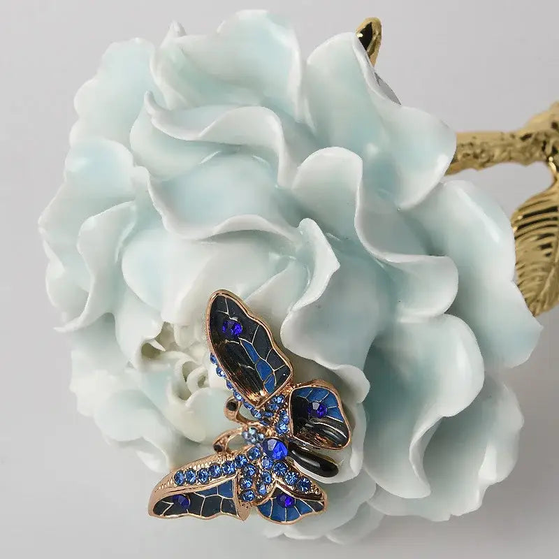 Luxury porcelain crystal rose decor featuring a delicate blue and black butterfly brooch with sparkling rhinestones