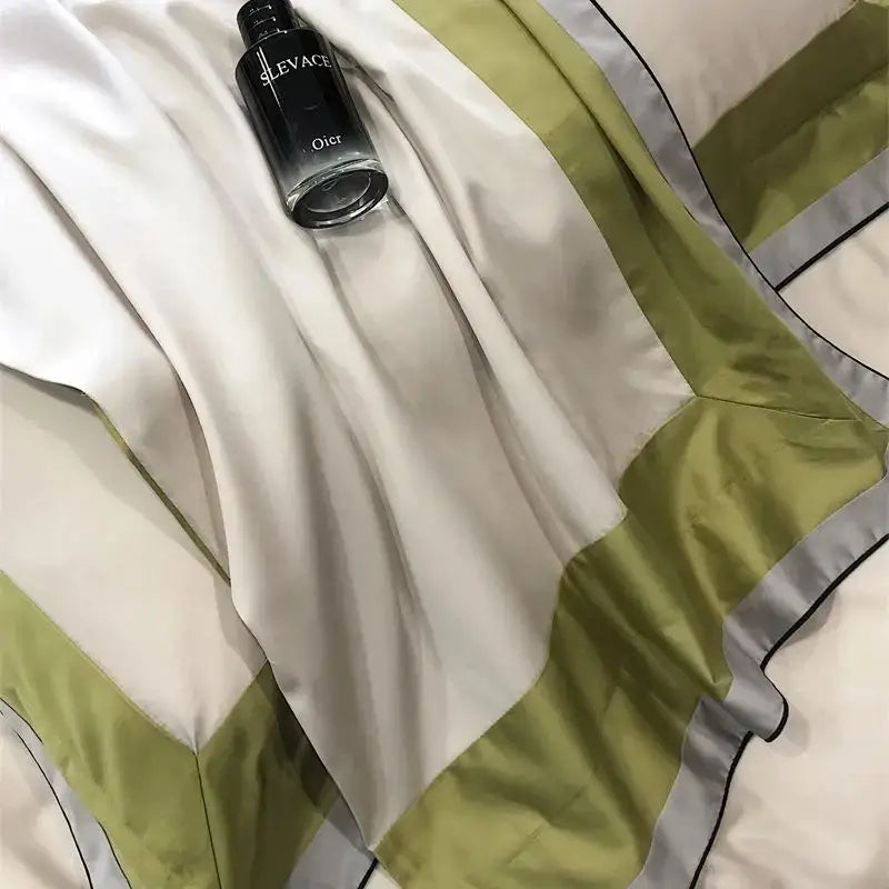 A sleek black glass dior sleevace perfume bottle with silver lettering beside a luxury sage green and cream 1000tc egyptian cotton bedding set