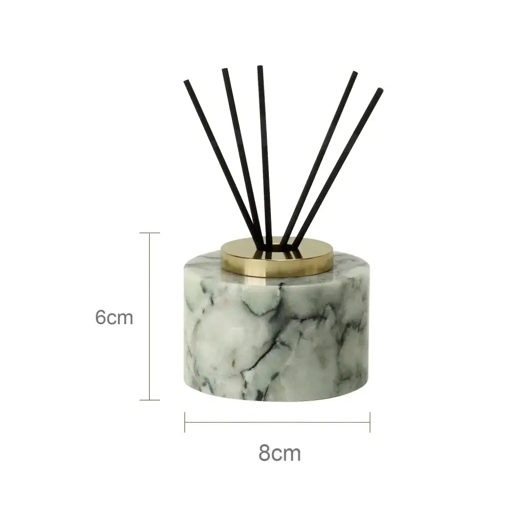 A sleek cylindrical reed diffuser with white and gold marble base and black reeds from emerald marble bathroom set