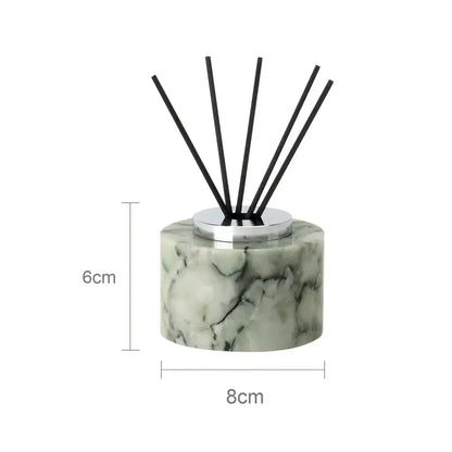 A sleek 6cm tall cylindrical reed diffuser with light green and white marble base and black reeds for emerald marble bathroom