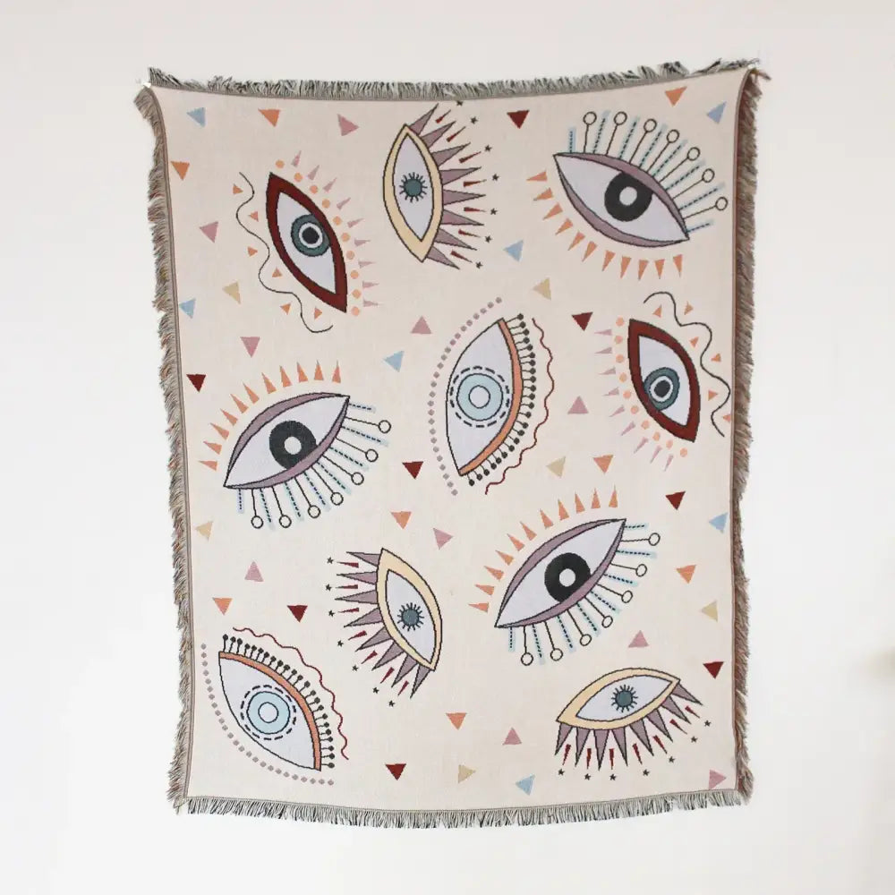 Cream-colored woven sofa cover with stylized eye pattern and geo tassel accents for picnic mat and living room use