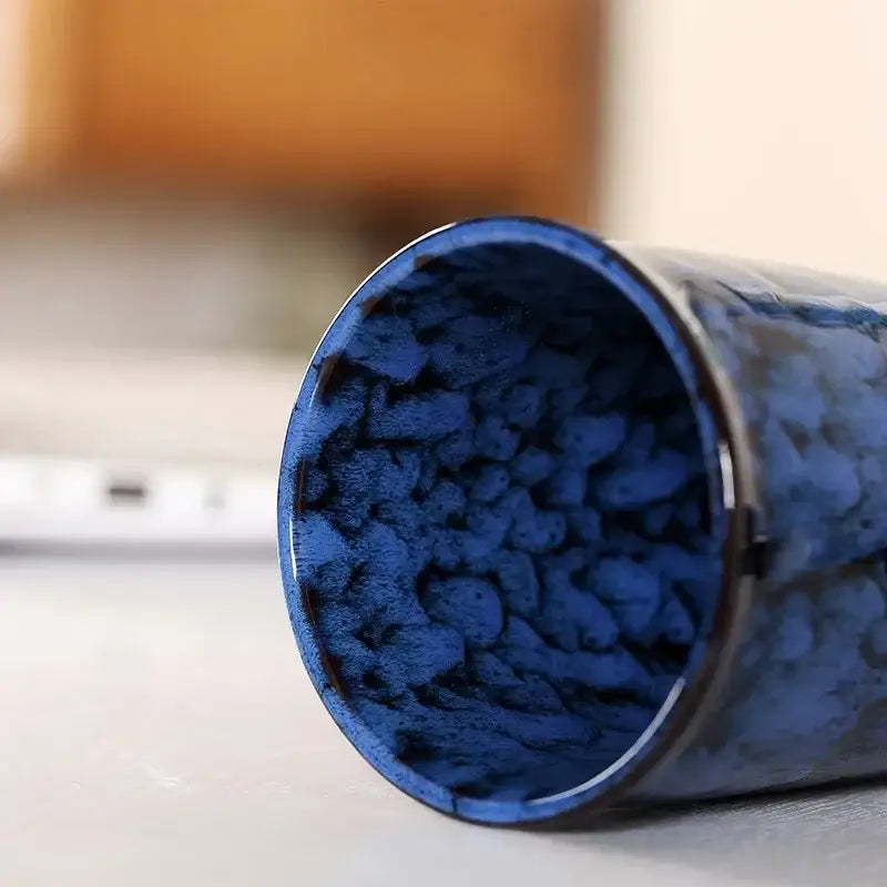 A cylindrical blue decorbites ceramic kiln mug filled with dark blue textured pebbles for kitchen travel use