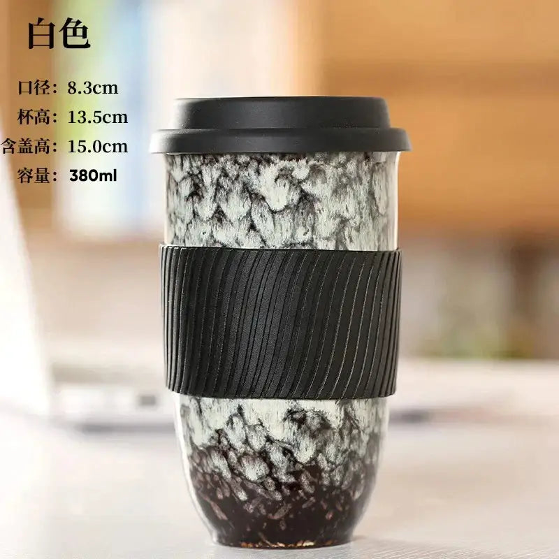 A white decorbites ceramic kiln mug with black lid and silicone grip featuring a darkening marbled pattern