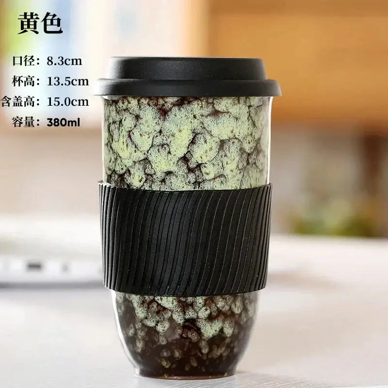 A yellow decorbites ceramic kiln mug with intricate crackled glaze and black silicone grip for travel or kitchen use
